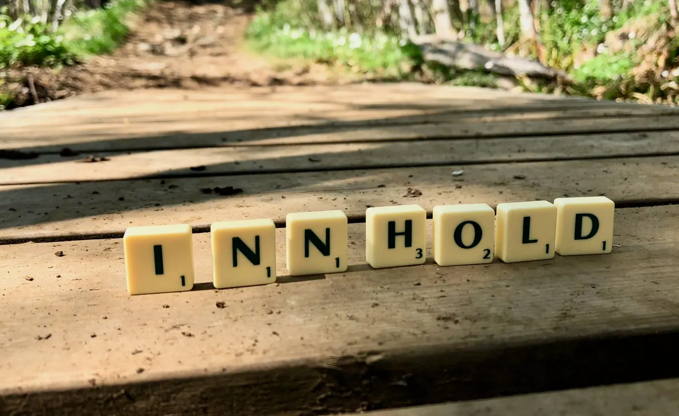 Scrabble-brikker lagt ut som ordet INNHOLD på en trebenk
