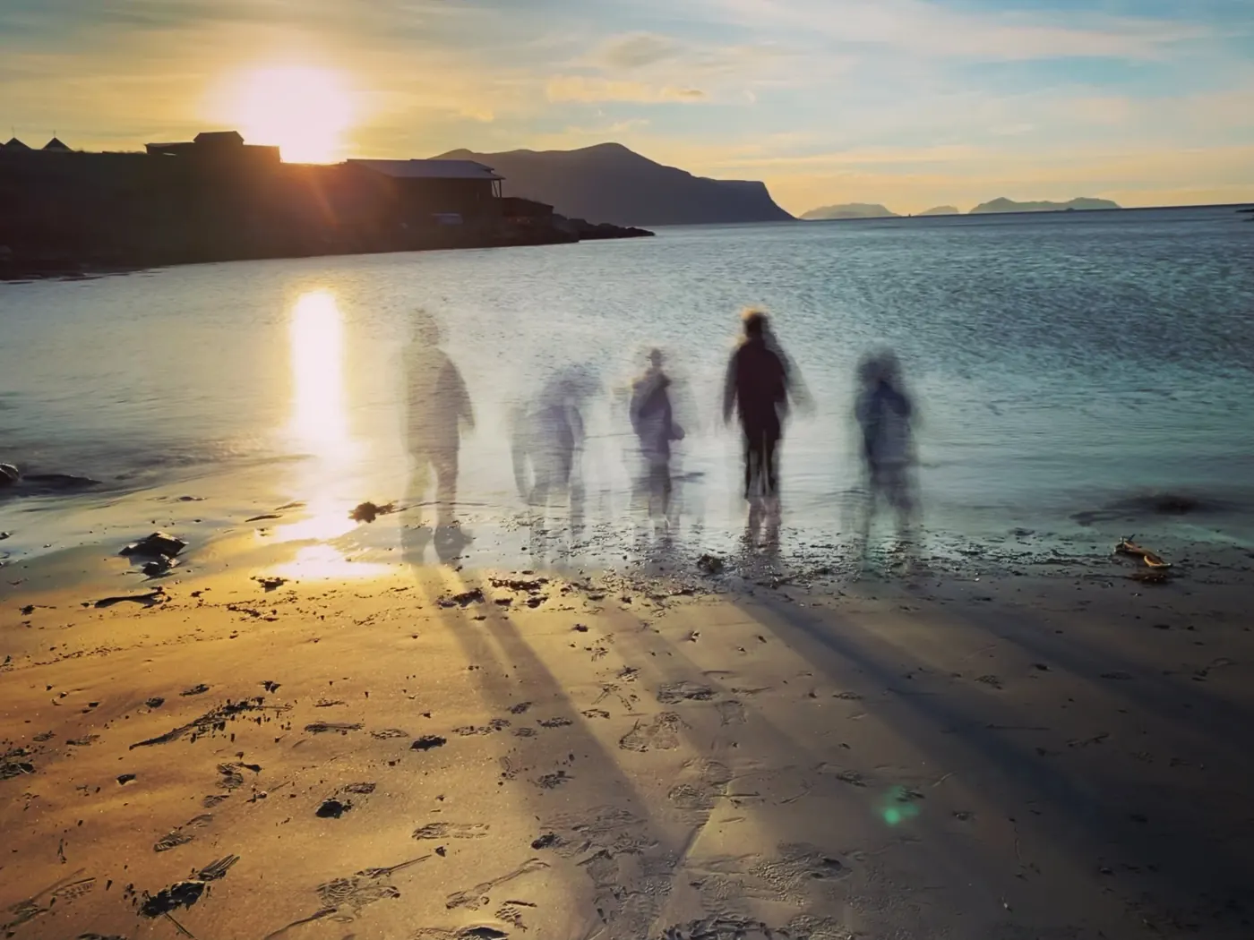 Silhuetter av mennesker i fjæra mot en solnedgang